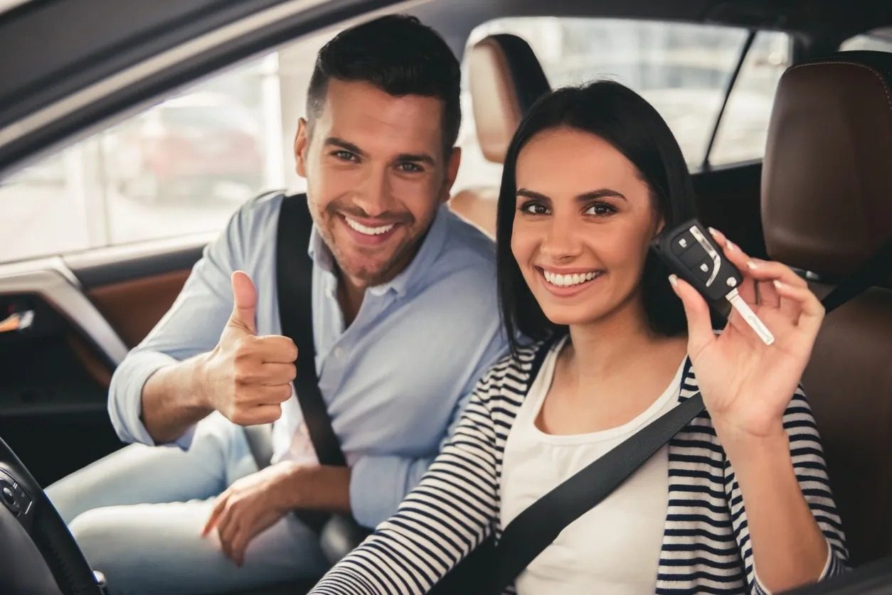 A smiling couple in their car holding up the keys